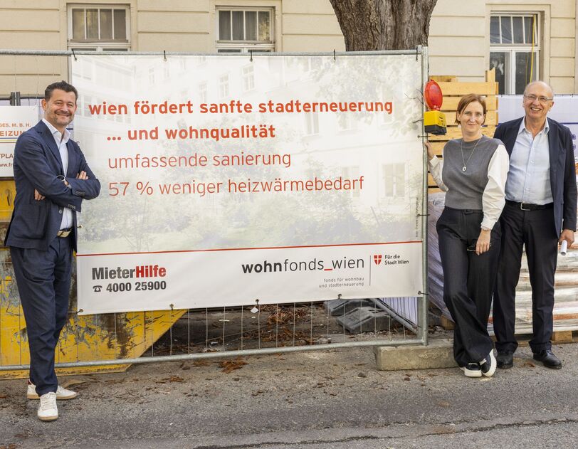 Drei Personen stehen vor einem Bauzaun mit einem Banner, das Informationen zur Stadtentwicklung und Wohnqualität in Wien zeigt