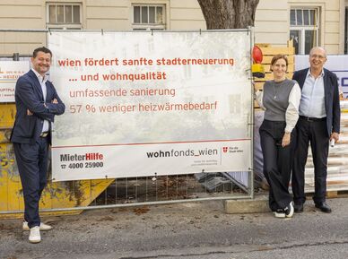 Drei Personen stehen vor einem Bauzaun mit einem Banner, das Informationen zur Stadtentwicklung und Wohnqualität in Wien zeigt