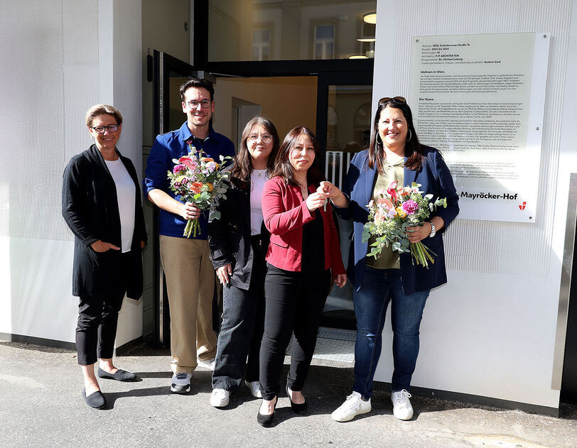 Wiener Wohnen Direktorin Karin Ramser, Bezirksvorsteher Michael Luxenberger und Vizebürgermeisterin und Wohnbaustadträtin Kathrin Gaál mit frisch eingezogenen Bewohnerinnen stehen vor dem Eingang des Gemeindebau NEU in der Schönbrunnerstraße. Kathrin Gaál überreicht der neuen Mieterin symbolisch ihren Wohnungsschlüssel. Sie hält dabei auch einen bunten Blumenstrauß in der Hand, ebenso wie der Bezirksvorsteher von Margareten