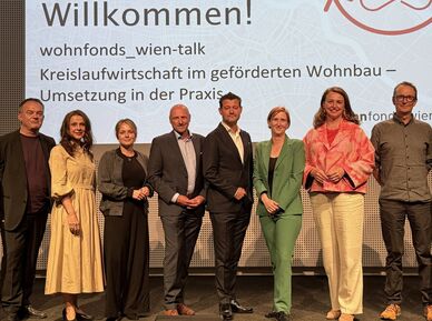 Gruppe von zehn Personen steht vor einer Präsentationswand mit dem Text 'Willkommen! wohnfonds_wien-talk Kreislaufwirtschaft im geförderten Wohnbau – Umsetzung in der Praxis'