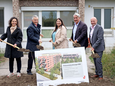 Katharina Klement (Vizedirektorin von Wiener Wohnen), Gemeinderat Josef Taucher, Vizebürgermeisterin und Wohnbaustadträtin Kathrin Gaál, Bezirksvorsteher Ernst Nevrivy und Paul Steurer, Direktor der WIGEBA, stehen jeweils mit einem Spaten voll Erde hinter einer Tafel mit der Visualisierung des Gemeindebau NEU in der Weidingergasse. Sie sind durchwegs herbstlich gekleidet und lächeln in die Kamera. 