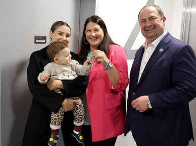 Vizebürgermeisterin und Wohnbaustadträtin Kathrin Gaál und Bezirksvorsteher Alexander Nikolai in der neuen Wohnhausanlage übergeben einer Frau mit Baby am Arm die Schlüssel zu ihrer neuen Wohnung.