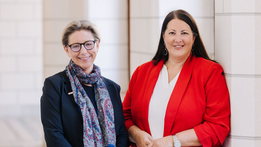 Zwei Frauen, Karin Ramser und Kathrin Gaál, stehen in einem Gang des Rathauses und lächeln in die Kamera. Beide sind businessmäßig mit Blazern gekleidet.